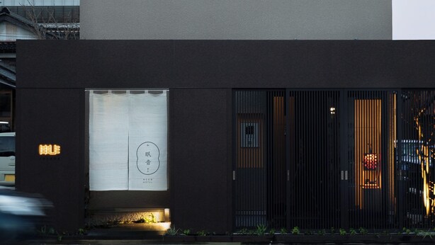 Un bâtiment moderne doté d’un toit plat, d’une grande fenêtre à motifs circulaires et d’une enseigne avec des caractères japonais.