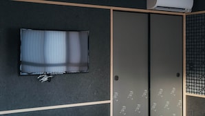 Une pièce dotée d’un téléviseur à écran plat fixé au mur, d’une porte coulissante ornée d’un motif et d’un appareil de climatisation installé au-dessus.