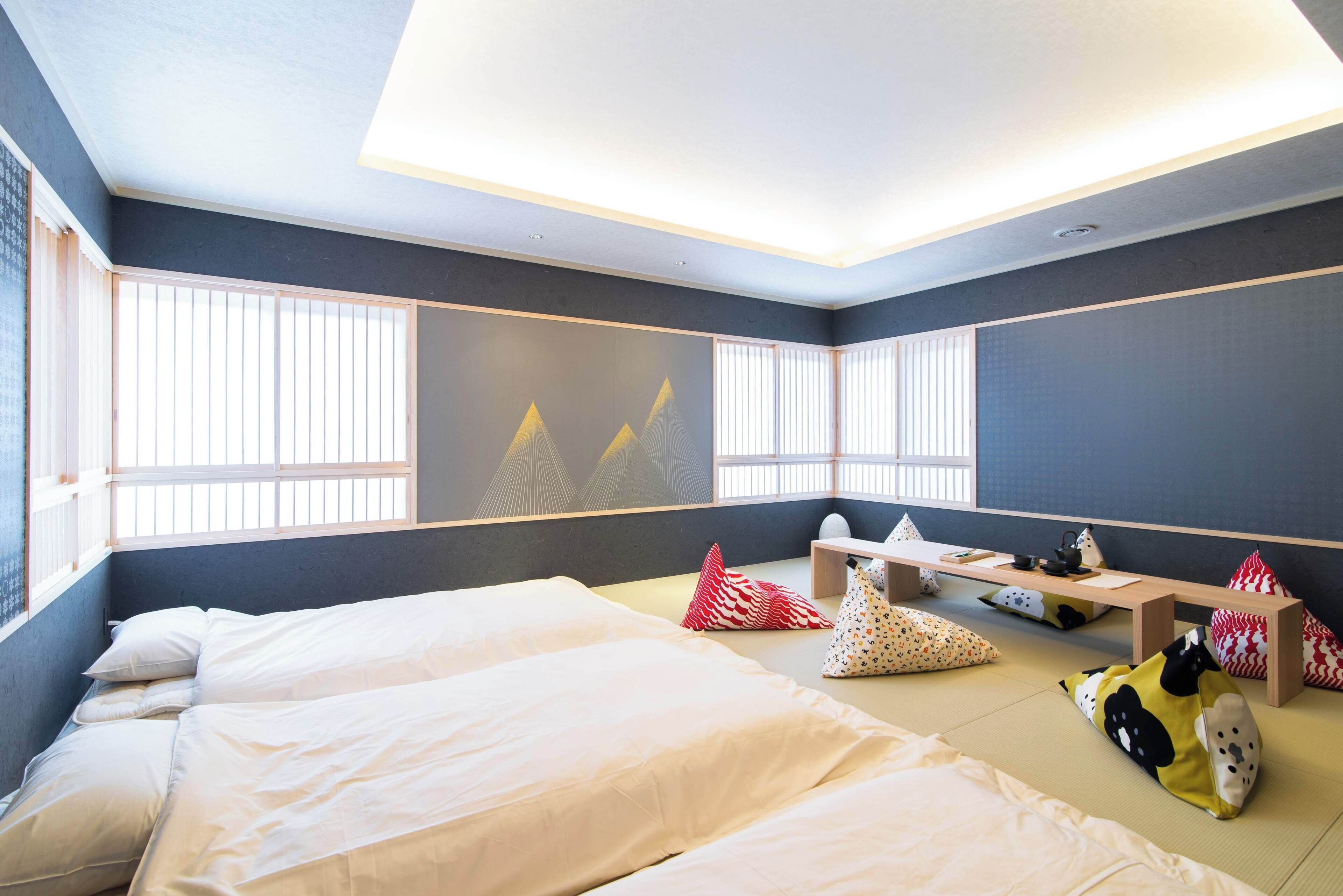A room with two beds, a desk, and a window with vertical blinds.
