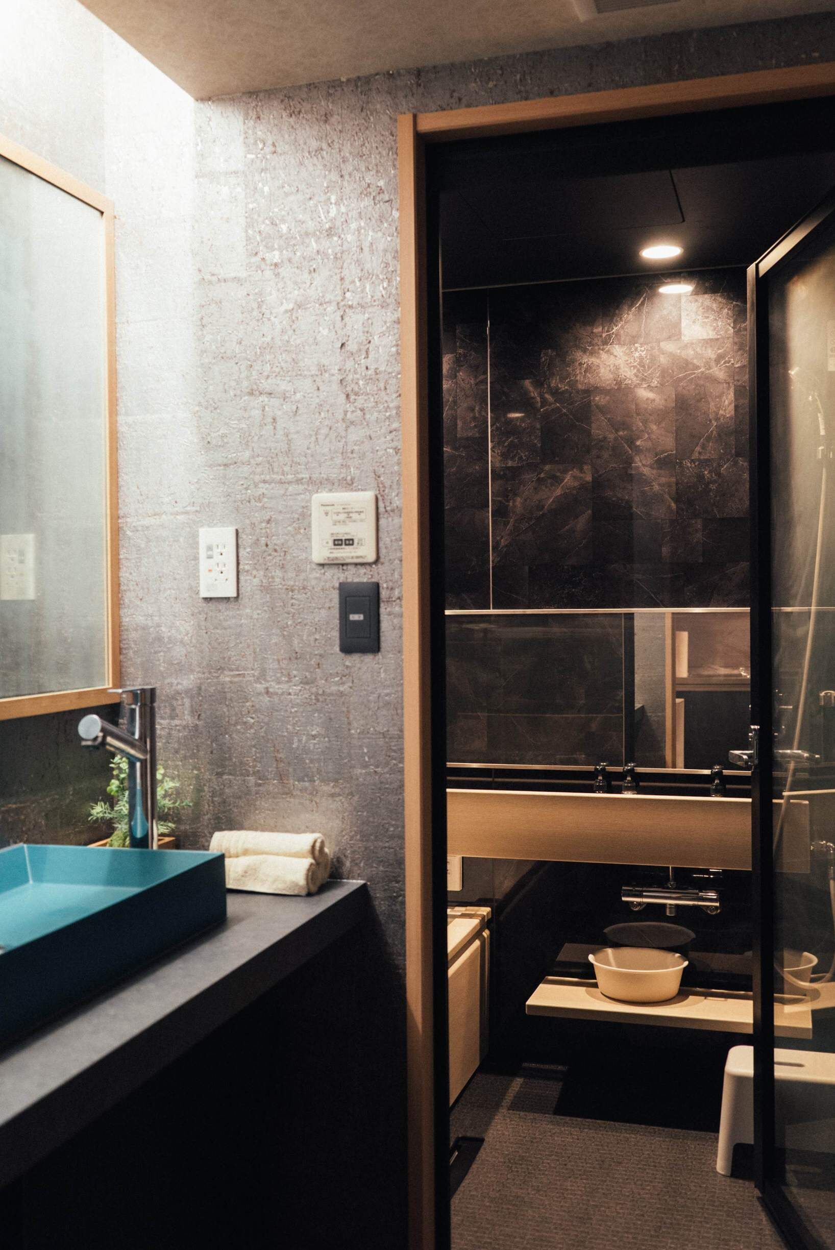 Un baño moderno con un espejo grande, un lavabo azul, una toalla y una zona de ducha.