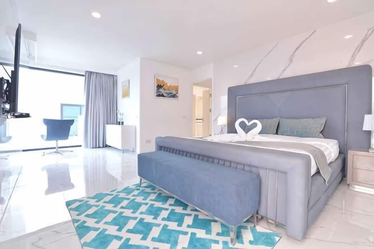 A modern bedroom with a large bed, a seating area, and a view of the city.