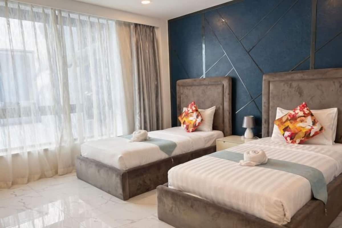 A hotel room with two beds, a large window with sheer curtains, a dark accent wall, and a marble floor.