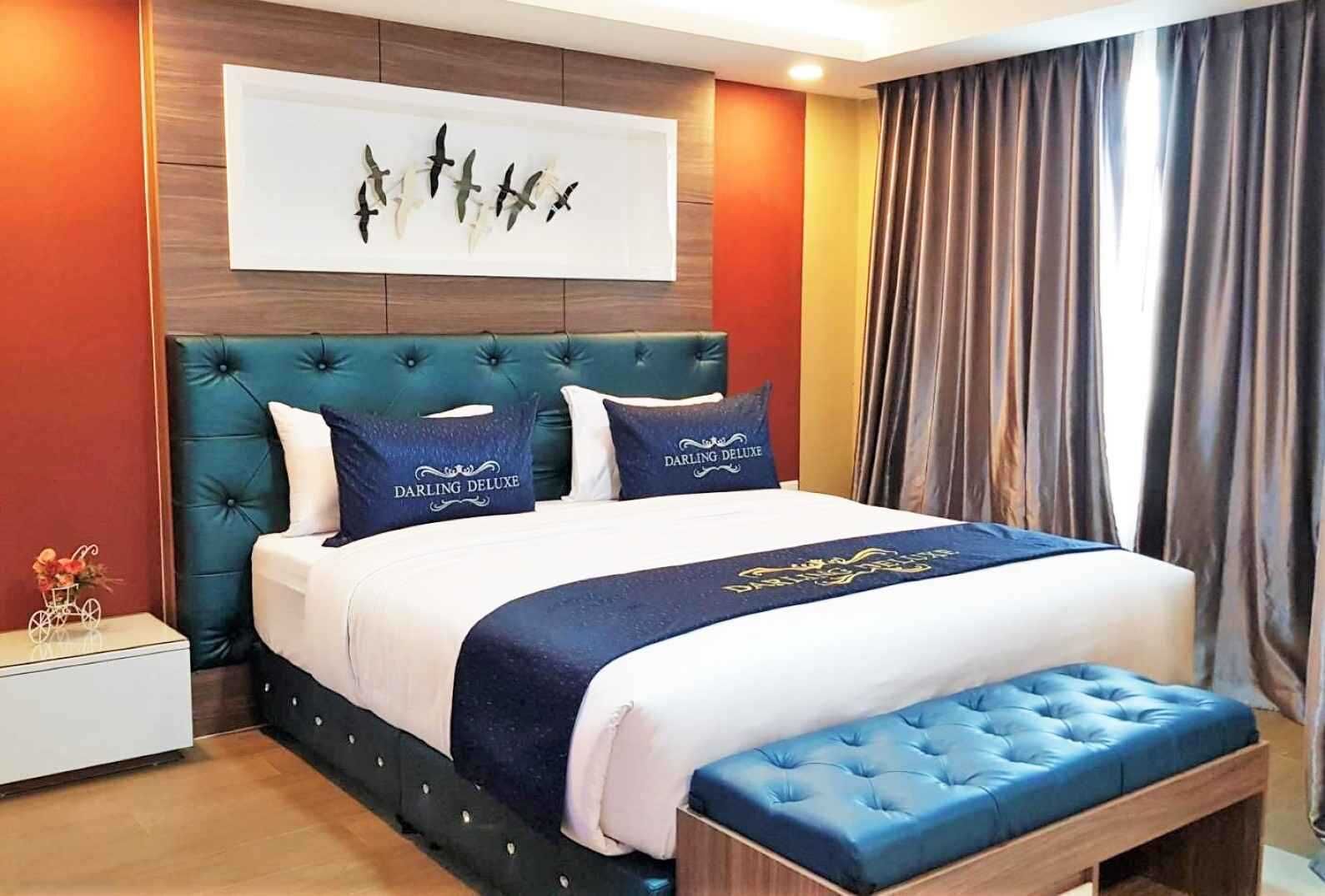 A hotel room with a large bed, a headboard, a bench, a nightstand, and a wall art piece.