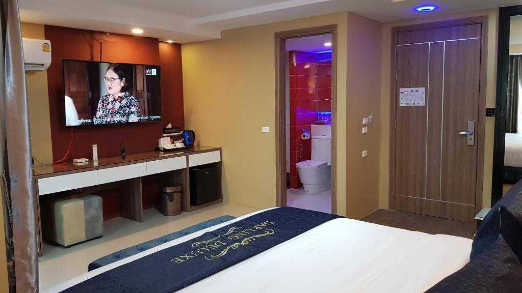 A hotel room with a bed, a TV mounted on the wall, a small desk with a chair, and a door leading to a bathroom.