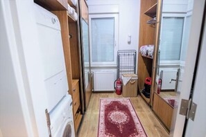 A compact bathroom with a washing machine, a radiator, a fire extinguisher, and a patterned rug.