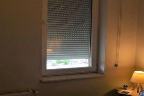 A room with a window with blinds, a radiator, and a lamp on a bedside table. - Gorgeous Two Bedroom Apartment - Roya (Istanbul)