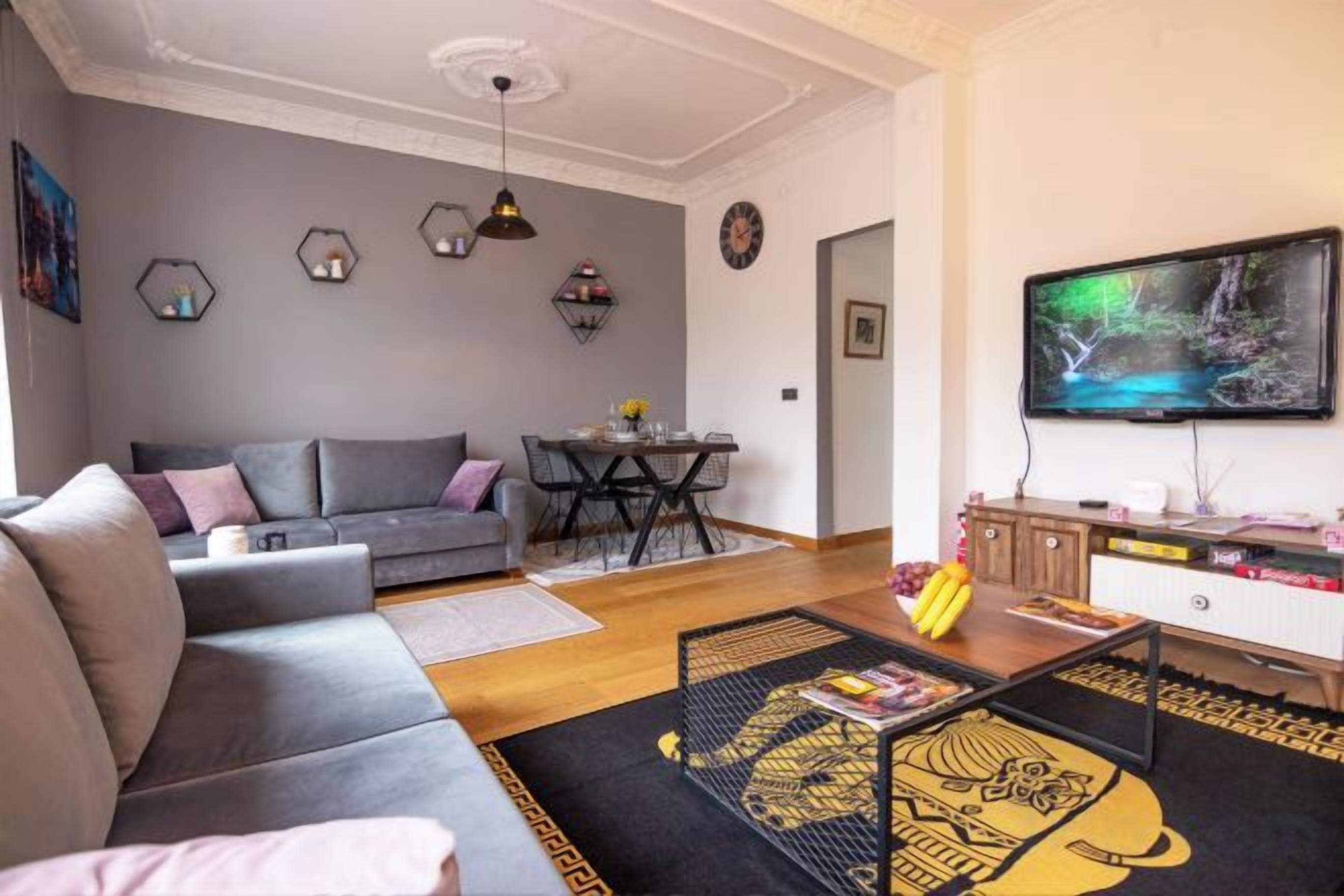 A modern living room with a grey sofa, a coffee table, and a flat-screen TV mounted on the wall.