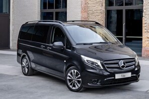 A black Mercedes-Benz Vito parked outside a building with a brick facade and large windows. - Gorgeous Two Bedroom Apartment - Roya (Istanbul)