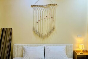 A bed with white bedding, a wall hanging with tassels, a lamp on a bedside table, and a curtain on the left. - Vietnam Travelers Home 1 with Private Balcony (Hanoi)