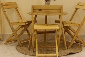 A wooden dining table with chairs, a vase with flowers, and a woven rug on the floor.