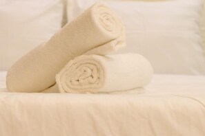 Una toalla beige bien doblada sobre una cama con un almohadón blanco.
