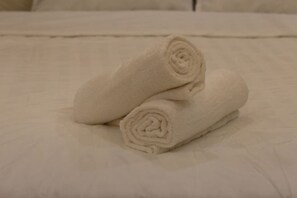 Una cama con sábana blanca y dos toallas enrolladas encima.
