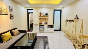 A compact living space with a sofa, a dining table, a kitchen area, and a shoe rack. - Vietnam Travelers Home 1 with Private Balcony (Hanoi)