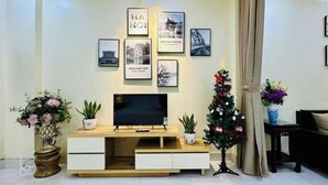 A living room with a TV on a wooden stand, a Christmas tree, and framed pictures on the wall. - Vietnam Travelers Home 1 with Private Balcony (Hanoi)