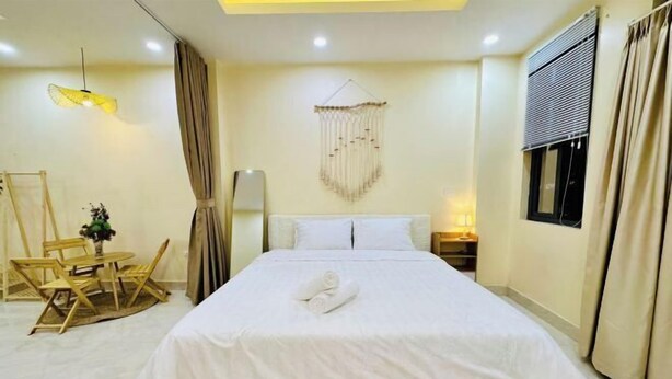 A hotel room with a bed, a desk, a chair, a hanging light fixture, and a window with curtains. - Vietnam Travelers Home 1 with Private Balcony (Hanoi)