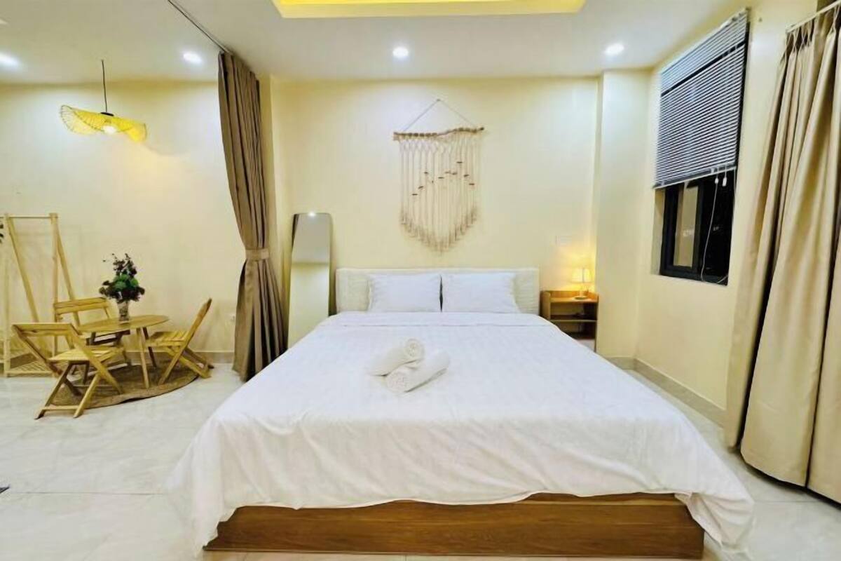 Habitación de hotel con cama, escritorio, silla, lámpara colgante y ventana con cortinas.