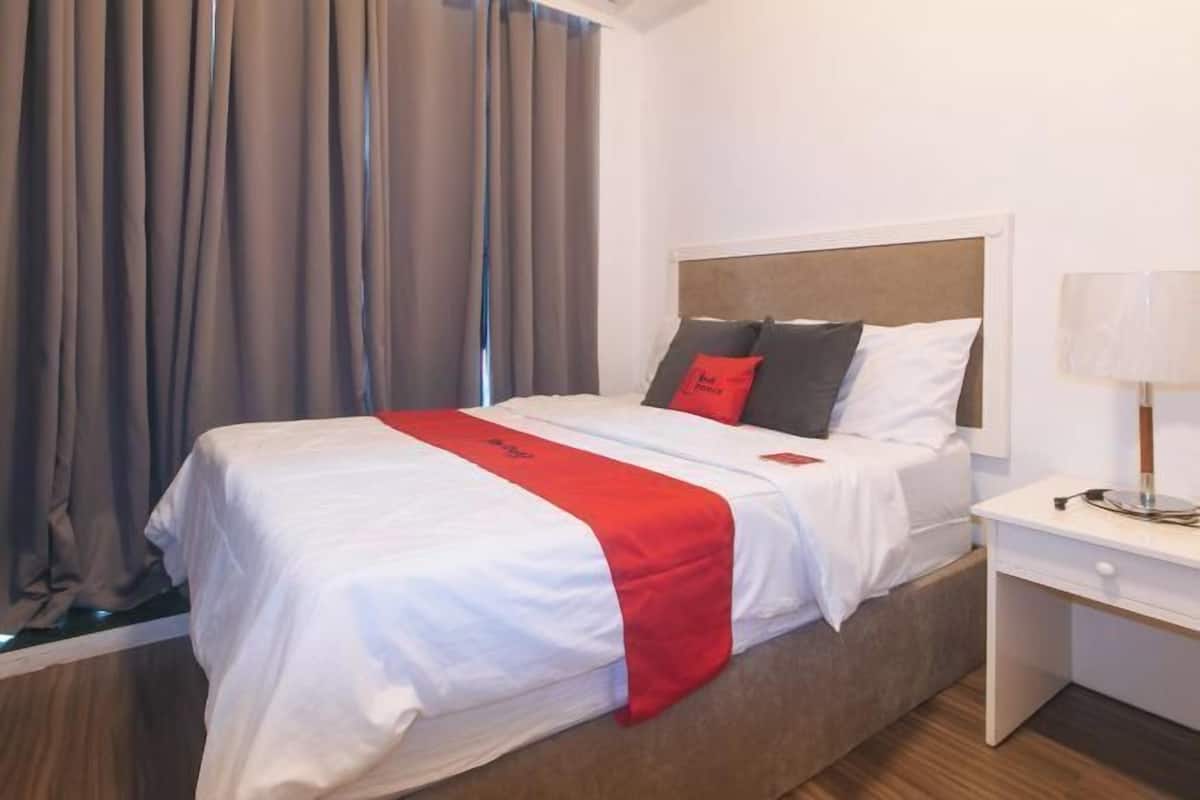 A hotel room with a bed, curtains, a bedside table, and a lamp.