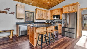 Une cuisine avec des meubles de rangement en bois, un réfrigérateur en acier inoxydable, un îlot central en bois avec des tabourets et un banc.