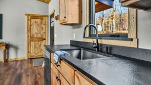 Une cuisine avec des meubles de rangement en bois, un plan de travail noir et une fenêtre donnant sur des arbres.