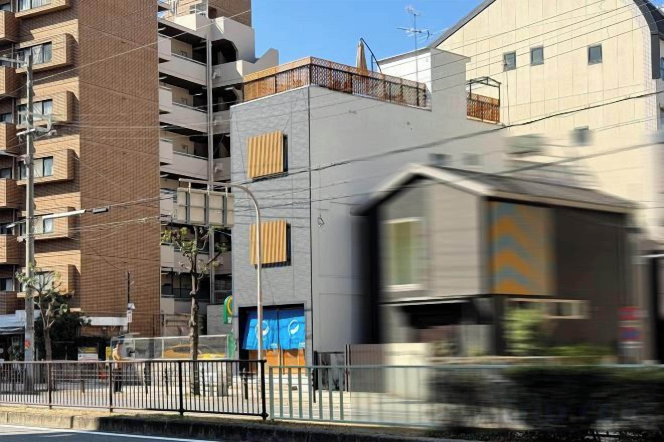 A train passing by a building with a modern design, a fence, and a clear sky.