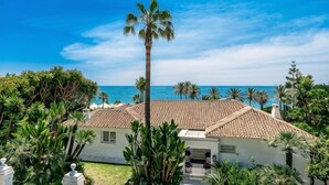 A coastal building with a tiled roof, surrounded by palm trees and a view of the sea. - All About Puente Romano Penthouse Suite (Marbella)