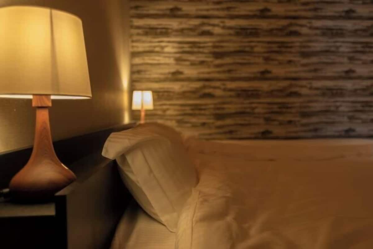 Un lit avec une tête de lit, une table de chevet avec une lampe et un mur orné d’un motif texturé.
