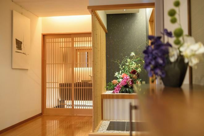 A traditional Japanese interior with a sliding door, a wooden floor, and a floral arrangement on a table.