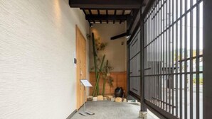 Un couloir avec une porte en bois, des plantes en bambou et un portail en métal noir.