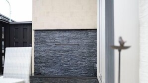 Un coin de pièce avec un mur en pierre, une chaise blanche et une porte dotée d’une poignée en métal.