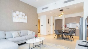 A modern living room with a grey sofa, a round coffee table, and a dining area with a table and chairs. - Mh- Act - Downtown 1BHK-Ref4002 (Dubai)
