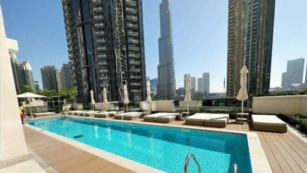 A rooftop pool with lounge chairs and umbrellas, surrounded by high-rise buildings. - Mh- Act - Downtown 1BHK-Ref4002 (Dubai)