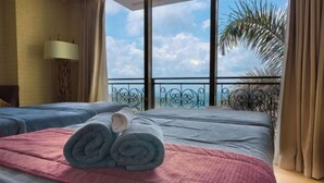 Habitación de hotel con dos camas, un balcón con vistas al cielo y palmeras, y una lámpara a la izquierda.