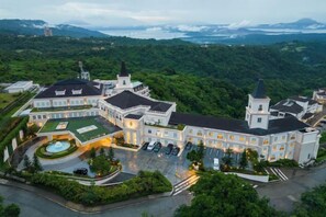 A large, multi-story hotel with a central courtyard, surrounded by lush greenery and a mountainous backdrop. - MCollection - Scenic Tagaytay Getaway with Taal Views (Batangas)