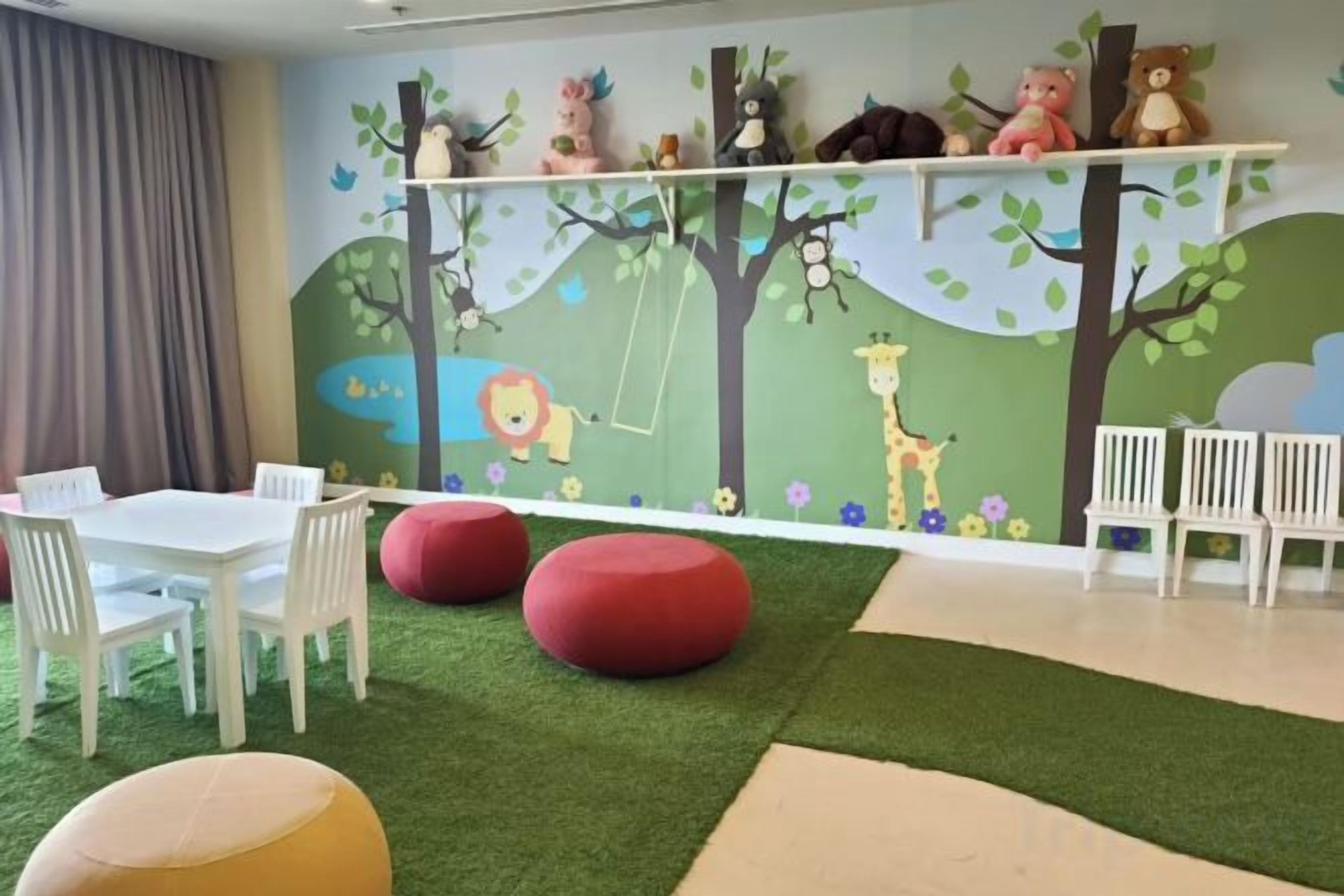 Espaço infantil com mural, assentos e grama sintética.