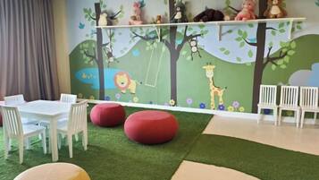 Espaço infantil com mural, assentos e grama sintética.