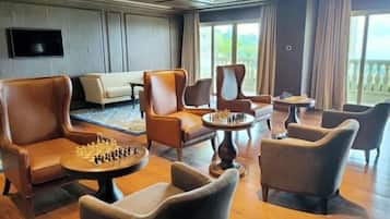 Quarto com poltronas de couro, um sofá, uma mesa de xadrez e uma janela grande com vista.