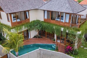 A modern villa with a swimming pool, wooden deck, and lush greenery.