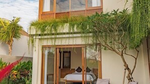 Een moderne slaapkamer met een bed, een glazen deur die leidt naar een balkon, en een zithoekje met kussens.