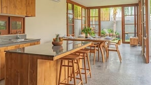 Een moderne keuken met houten kastjes, een centraal eiland met krukken, en grote ramen voor veel natuurlijk licht.