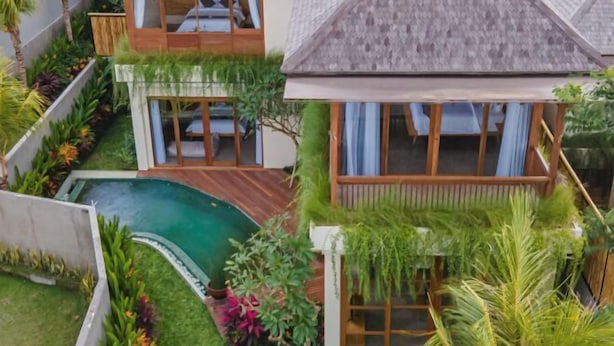 Een tweelaags huis met een zwembad, houten terras en weelderige begroeiing.