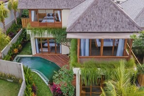 Een tweelaags huis met een zwembad, houten terras en weelderige begroeiing.
