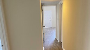 Un couloir avec un plancher en bois, des murs blancs et une porte blanche au fond.