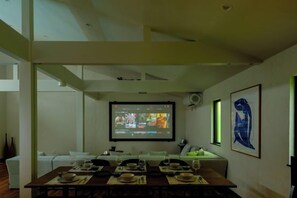A dining area with a long table set for a meal, a projector screen displaying a presentation, and artwork on the walls. - Syla Hotel Pool Villa (Yokosuka)