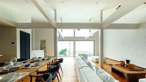 Un espace de repas moderne avec une longue table dressée pour un repas, un canapé et une vue dégagée grâce à de grandes fenêtres.