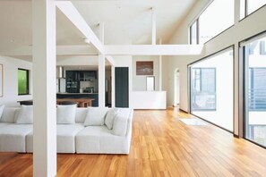Un'ampia zona giorno con un divano bianco, pavimento in legno e grandi finestre.