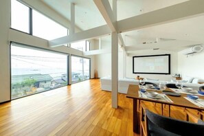 Un'area pranzo moderna con un tavolo in legno apparecchiato per un pasto, ampie finestre con vista sulla città e un divano bianco sullo sfondo.