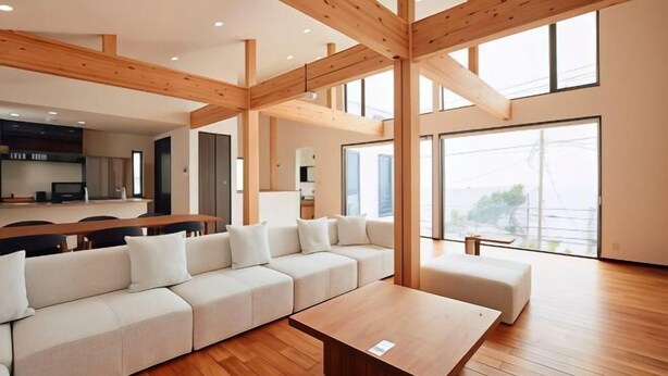 Un vaste espace de vie doté d’un plafond avec une grande poutre en bois, d’un canapé d’angle, d’une table basse en bois et d’une vue dégagée grâce à de grandes fenêtres.