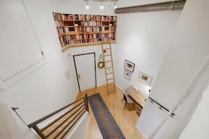 Une pièce avec un escalier en bois, un bureau avec une chaise, une bibliothèque et une porte.