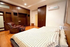 A bedroom with a bed, a leather chair, a wardrobe, and an air conditioning unit. - Decozy 3.0 Semi-D (18pax++) (Ipoh)