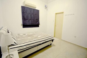 A bedroom with a bed, bedside table, lamp, air conditioning unit, and a door. - Decozy 3.0 Semi-D (18pax++) (Ipoh)